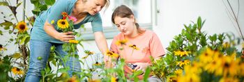 Ein Mädchen und eine Erwachsene kümmern sich um die Pflege der Blumen im Garten