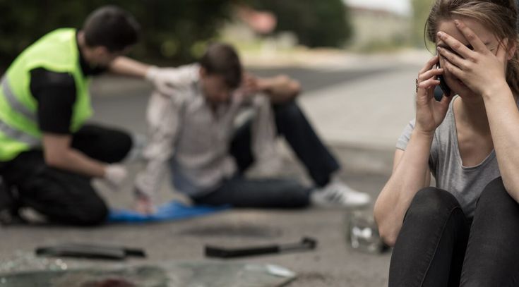Verzweifelte junge Autofahrerin sitzt nach einem Verkehrsunfall auf der Straße und telefoniert