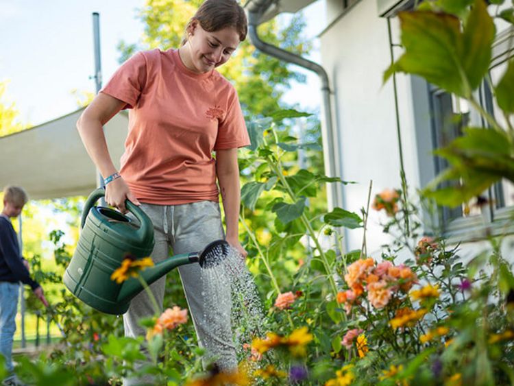 Ein Mädchen gießt die Blumen im Garten