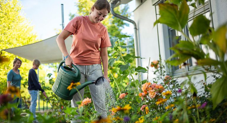 Ein Mädchen gießt die Blumen im Garten