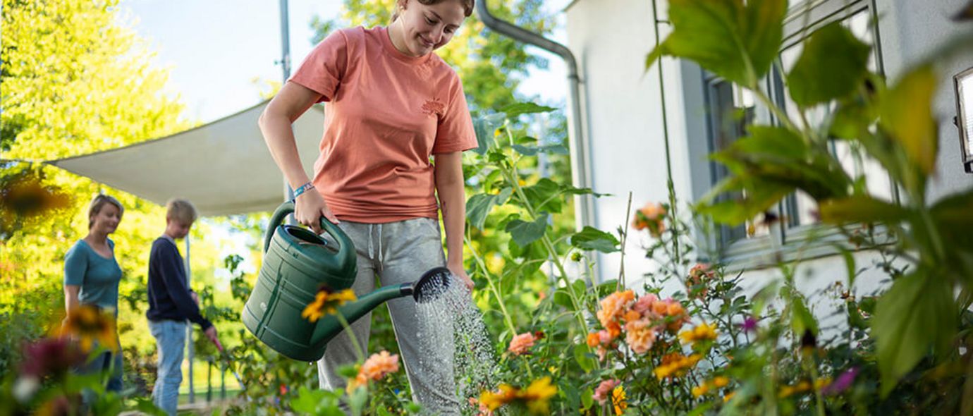 Ein Mädchen gießt die Blumen im Garten