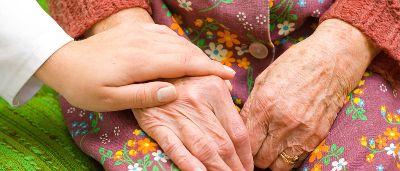  Eine Ärztin legt ihre Hand auf die einer älteren Frau
