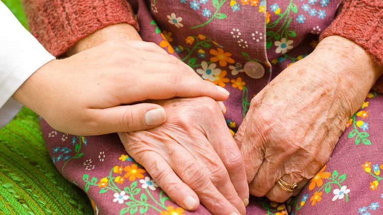  Eine Ärztin legt ihre Hand auf die einer älteren Frau