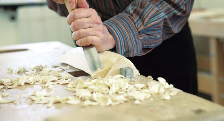 Ein Patient bearbeitet Holz mit dem Hobel in der Werkstatt