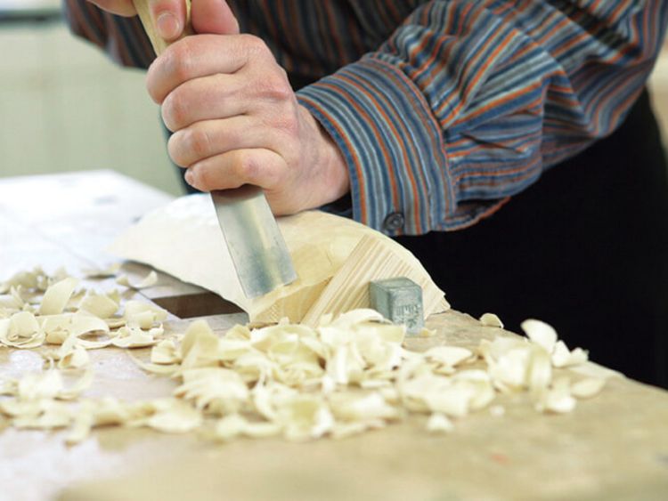 Ein Patient bearbeitet Holz mit dem Hobel in der Werkstatt