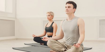 Ein Mann und eine Frau sitzen nebeneinander im Lotussitz auf einer Matte und meditieren