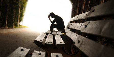 Ein Patient sitzt gedankenverloren auf einer Bank im Wald und hält die Hand an die Stirn